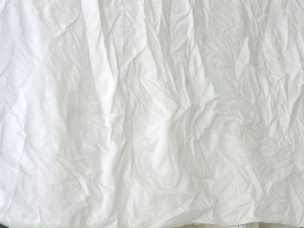 a wrinkled and worn white flat sheet