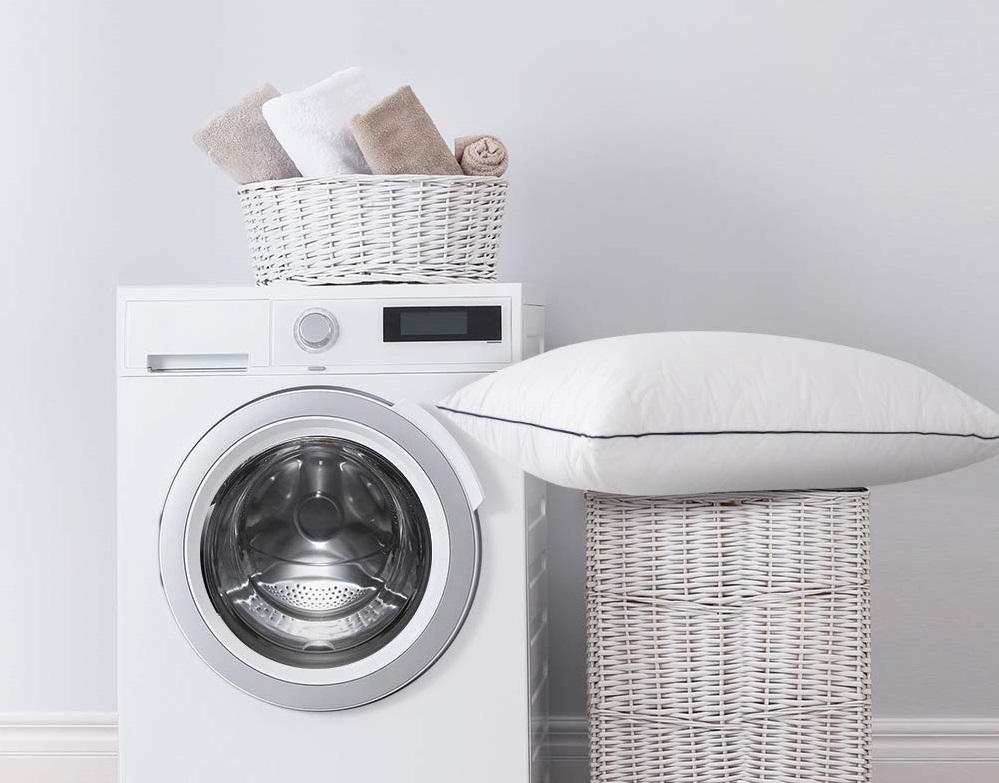 a laundry room featuring a washing machine, basket, and a bed pillow