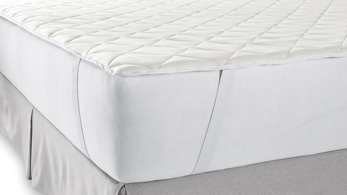 the corner of a bed, showing a mattress pad with the straps looped around the corner