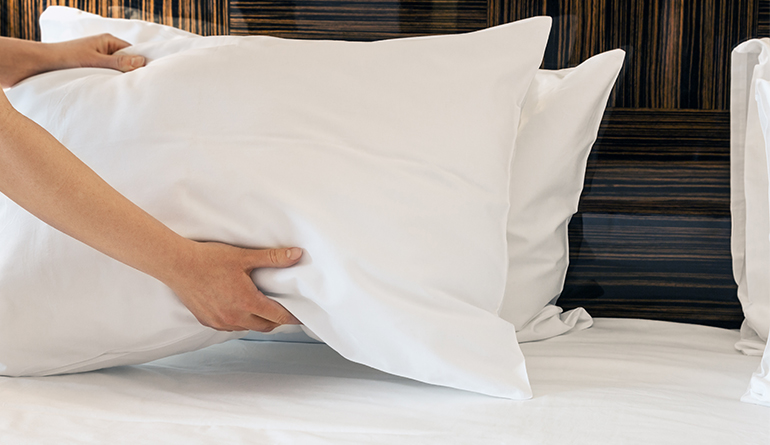 a woman fluffing pillows on top of a bed