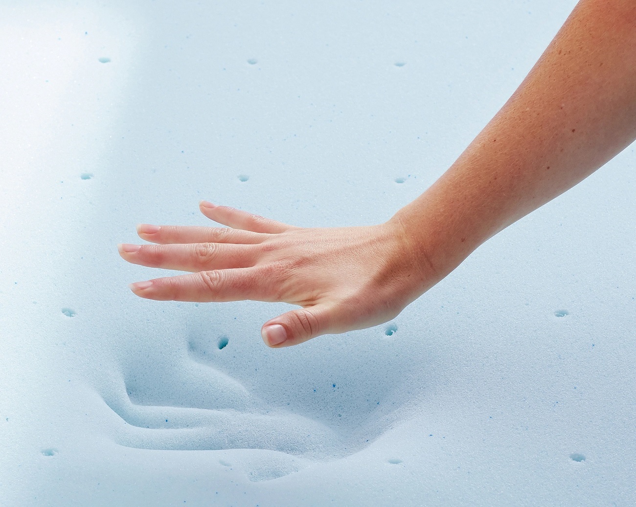 a woman pressing her hand on a foam mattress topper