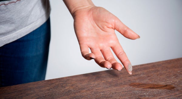 a woman running her finger over a dusty piece of wood furniture