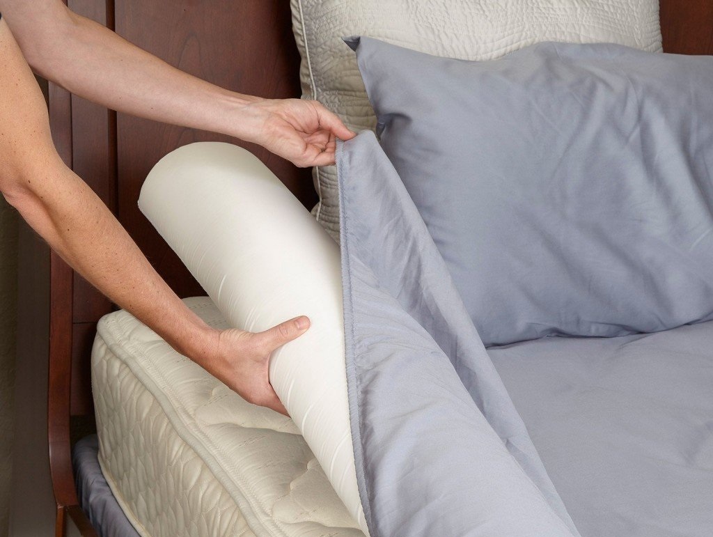 a woman placing a bed bumper on a bed, under a fitted sheet