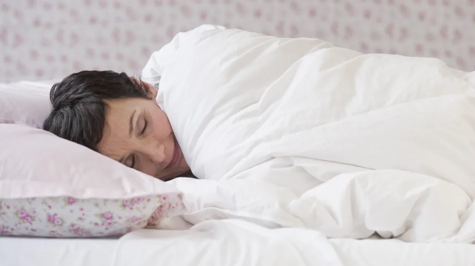a woman sleeping in bed with a comforter