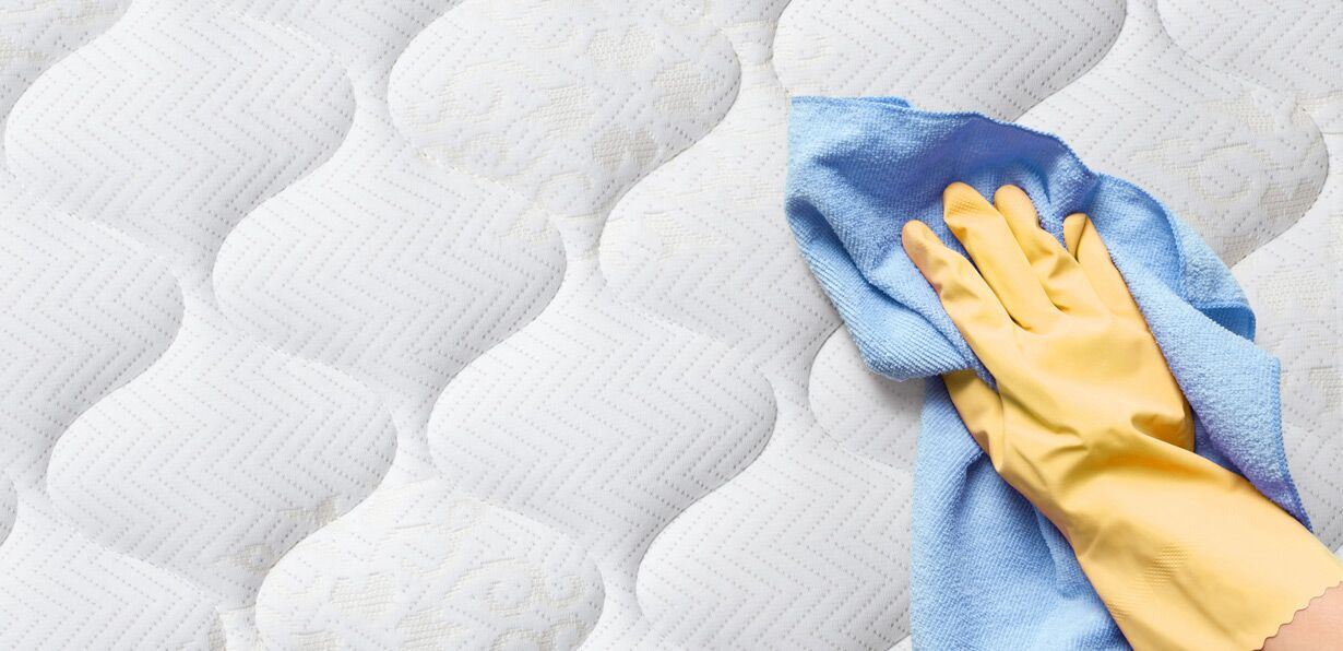 a woman wearing gloves and wiping the surface of a bed